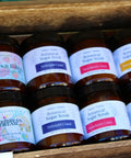 Eight Botanical Sugar Scrub jars in a wooden crate, showing Berries n Bubbly, Caribbean Dream, Midnight Coast, Strawberry Coco, and Pineapple Papaya scents