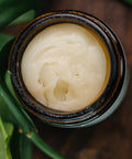 Close-up of open Serenity Magnesium Cream jar showing creamy texture, with green leaves in the background
