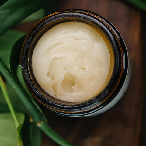 Close-up of open Serenity Magnesium Cream jar showing creamy texture, with green leaves in the background