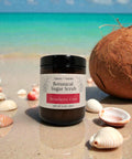 Botanical Sugar Scrub jar in Strawberry Coco scent on a sandy beach with seashells and a coconut