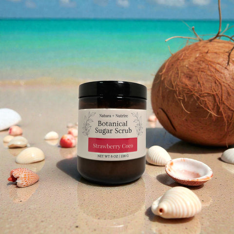 Botanical Sugar Scrub jar in Strawberry Coco scent on a sandy beach with seashells and a coconut