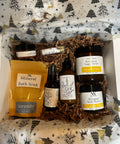 Gift box with Natura+Nutrire products including Silky Soft Whipped Body Butter, Mineral Bath Soak, Botanical Sugar Scrub, and a rollerball, nestled in a holiday-patterned box liner