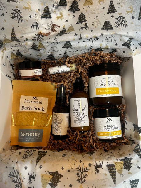 Gift box with Natura+Nutrire products including Silky Soft Whipped Body Butter, Mineral Bath Soak, Botanical Sugar Scrub, and a rollerball, nestled in a holiday-patterned box liner