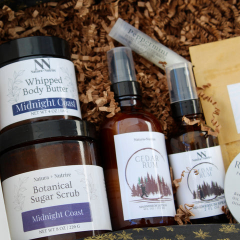 Natura+Nutrire gift collection with Whipped Body Butter, Botanical Sugar Scrub, and Cedar Rum Magnesium Lotion and Spray, nestled in brown crinkle paper