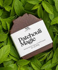 Patchouli Magic Vegan Soap bar with kraft paper label resting on a bed of green leaves