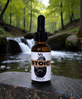 Stoic Beard Oil bottle on a rock beside a forest stream with a small waterfall