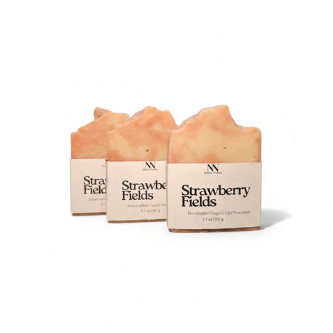 Three Strawberry Fields Handcrafted Soap bars wrapped in kraft paper sleeves, side by side on a white background