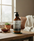 Cedar Rum Magnesium Lotion pump bottle on a wooden table with a steaming bowl of cinnamon sticks, a small succulent plant, and a cozy throw blanket by a window