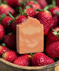 Strawberry Fields Handcrafted Soap bar in a wooden bowl surrounded by fresh strawberries