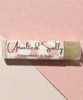Unsalted Sally Fragrance-Free Olive Oil Lip Balm tube on a pink and beige geometric background