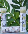 Three Olive Oil Lip Balm tubes - The Tropics, Lavender Lemonade, and Unsalted Sally - standing and lying in front of green leaves