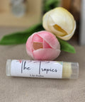 Tropics Pineapple Olive Oil Lip Balm tube labeled 'The Tropics' next to pink and yellow tulips on a linen surface