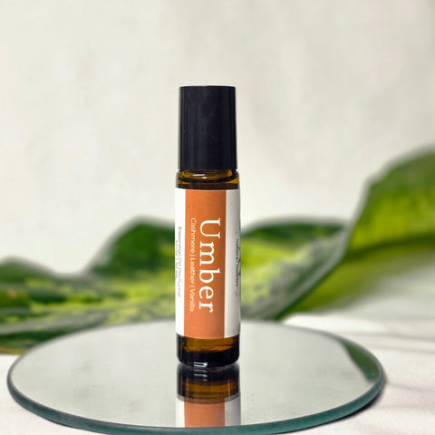 Umber Natural Botanical Fragrance rollerball bottle standing on a mirrored surface with green leaves in the background