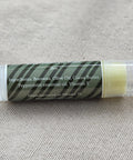 The OG Peppermint Lip Balm tube showing ingredients label listing beeswax, olive oil, cocoa butter, peppermint essential oil, and vitamin E