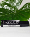 Obsidian Natural Botanical Fragrance rollerball bottle lying on its side in front of a large green leaf