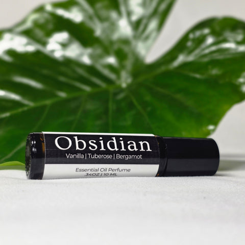 Obsidian Natural Botanical Fragrance rollerball bottle lying on its side in front of a large green leaf