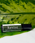 Revive Essential Oil Roller bottle lying on a large green leaf