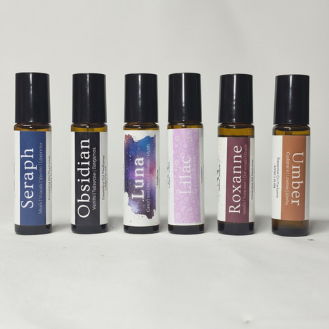 Body Oil Perfume rollerball bottles lineup: Seraph, Obsidian, Luna, Lilac, Roxanne, and Umber, on a white background
