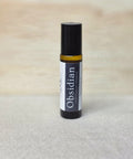 Body Oil Perfume Obsidian rollerball bottle standing on a light wood surface with linen backdrop