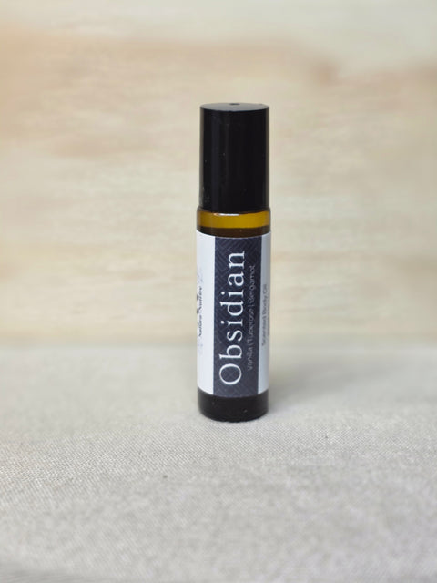 Body Oil Perfume Obsidian rollerball bottle standing on a light wood surface with linen backdrop