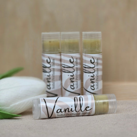 Four Vanille Vanilla Solid Perfume tubes arranged with a white tulip on a neutral background