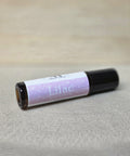 Body Oil Perfume Lilac rollerball bottle lying on its side on a linen surface