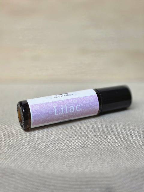 Body Oil Perfume Lilac rollerball bottle lying on its side on a linen surface