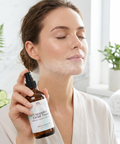 Woman applying Cucumber Facial Toner with Rice Ceramides to her neck in a bathroom, with fresh cucumber slices and a fern in the background