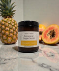 Botanical Sugar Scrub jar in Pineapple Papaya scent on a marble surface with a fresh pineapple and sliced papaya