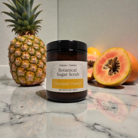 Botanical Sugar Scrub jar in Pineapple Papaya scent on a marble surface with a fresh pineapple and sliced papaya