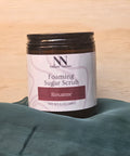 Foaming Sugar Scrub jar in Roxanne scent on a light wood surface with teal fabric
