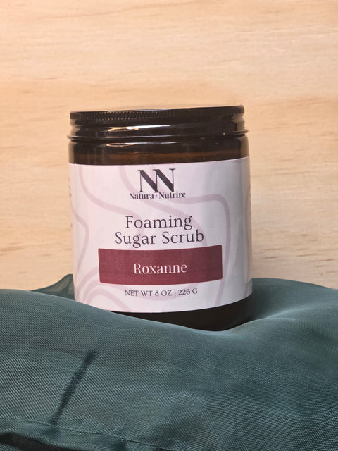 Foaming Sugar Scrub jar in Roxanne scent on a light wood surface with teal fabric