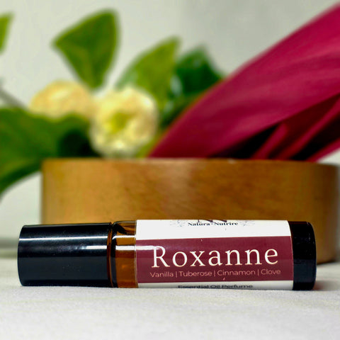 Roxanne Natural Botanical Fragrance rollerball bottle lying in front of a wooden bowl with white and pink flowers