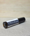 Body Oil Perfume Obsidian rollerball bottle lying on its side on a linen surface