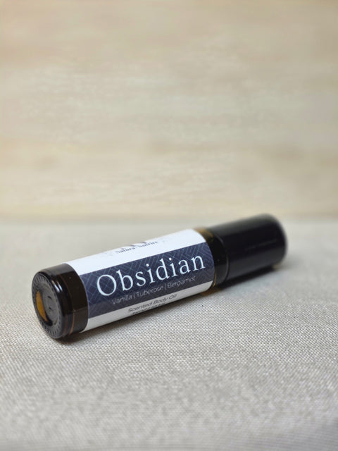 Body Oil Perfume Obsidian rollerball bottle lying on its side on a linen surface