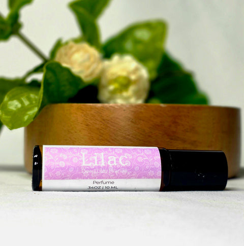 Lilac Natural Botanical Fragrance rollerball bottle lying in front of a wooden bowl and white lilac blossoms