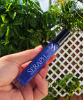 Hand holding the Seraph Handcrafted Non-Toxic Fragrance spray bottle against a lush green outdoor backdrop