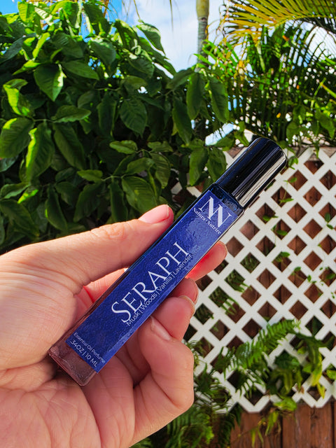 Hand holding the Seraph Handcrafted Non-Toxic Fragrance spray bottle against a lush green outdoor backdrop
