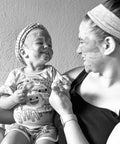 Black and white photo of a mother and toddler smiling together, both with Rose Renewal Clay Face Mask applied to their faces