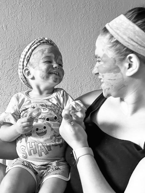 Black and white photo of a mother and toddler smiling together, both with Rose Renewal Clay Face Mask applied to their faces